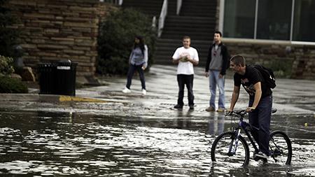 Junior Mechanical Engineering Garret Ehrick rides his bike near the enterence of the Lory Student Center Wednesday evening. Areas around Fort Collins including the CSUs campus flooded Wedneday evening during a rainstorm.