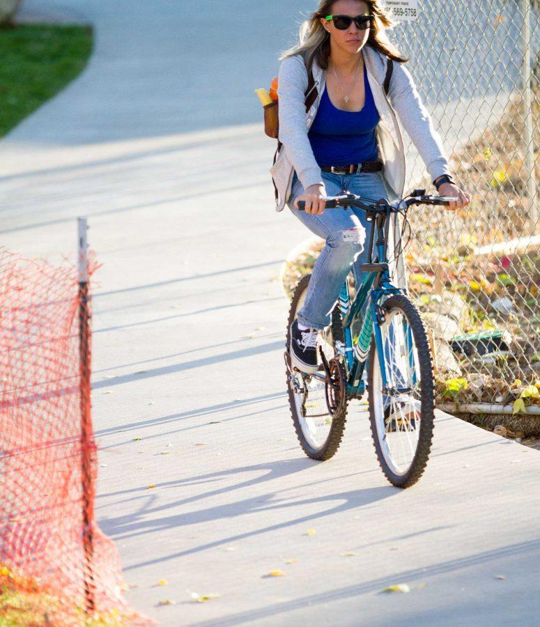 Junior Liz Torrez rides her bike through the construction filled sidewalk outside of Braiden Hall Tuesday afternoon. There are multiple large construction projects going on through campus this year.
