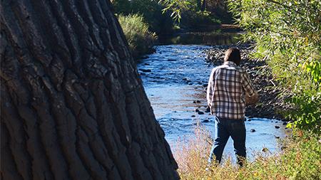 Andrew Dobersen walks along the Poudre River on Sunday afternoon. The river is running black with ash due to the infamous fires of this past summer.