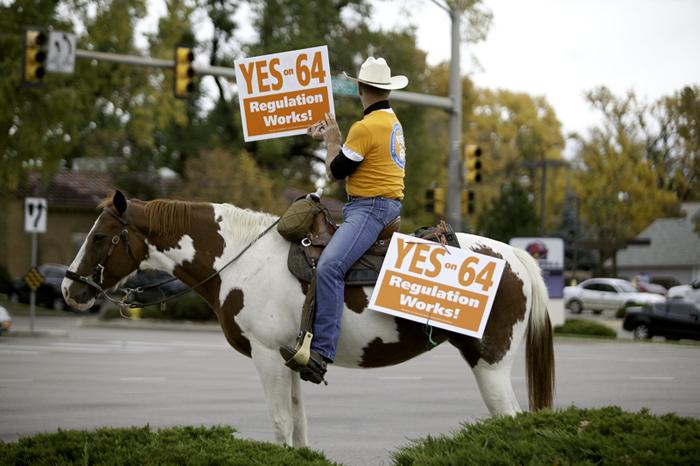 Retired police officer Howard Cowboy Wooldridge holds up a politcal sign saying Yes on 64 on top of his horse Tuesday morning on the corner of Prospect and College. Wooldrige is a police voice on capitol hill in opposition to drug prohibition.
