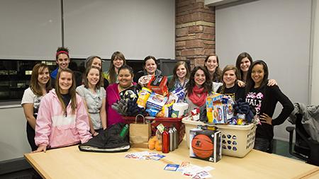 A group of Human Development and Family Studies students stand aroudn the Thanksgiving baskets they put together for two families. The baskets included items such as winter coats for kids, hot chocolate, and water bottles.