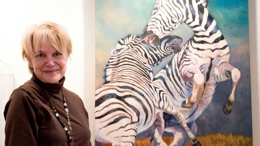 Karen Cannon stands before her painting titled "Stallions of the Serengeti" at the Poudre Studio of Artists and Galleries on Thursday afternoon. Cannon has been a PSA member for six months and has three of her works on display at the gallery.