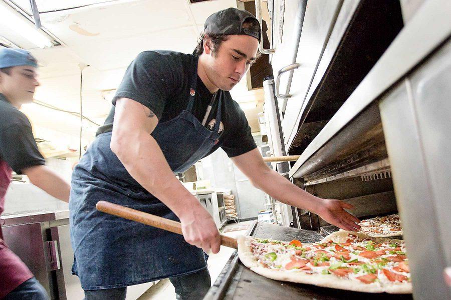 Zachary Hunter carefully places two pizzas in the oven at Pizza Casbah Wednesday night.