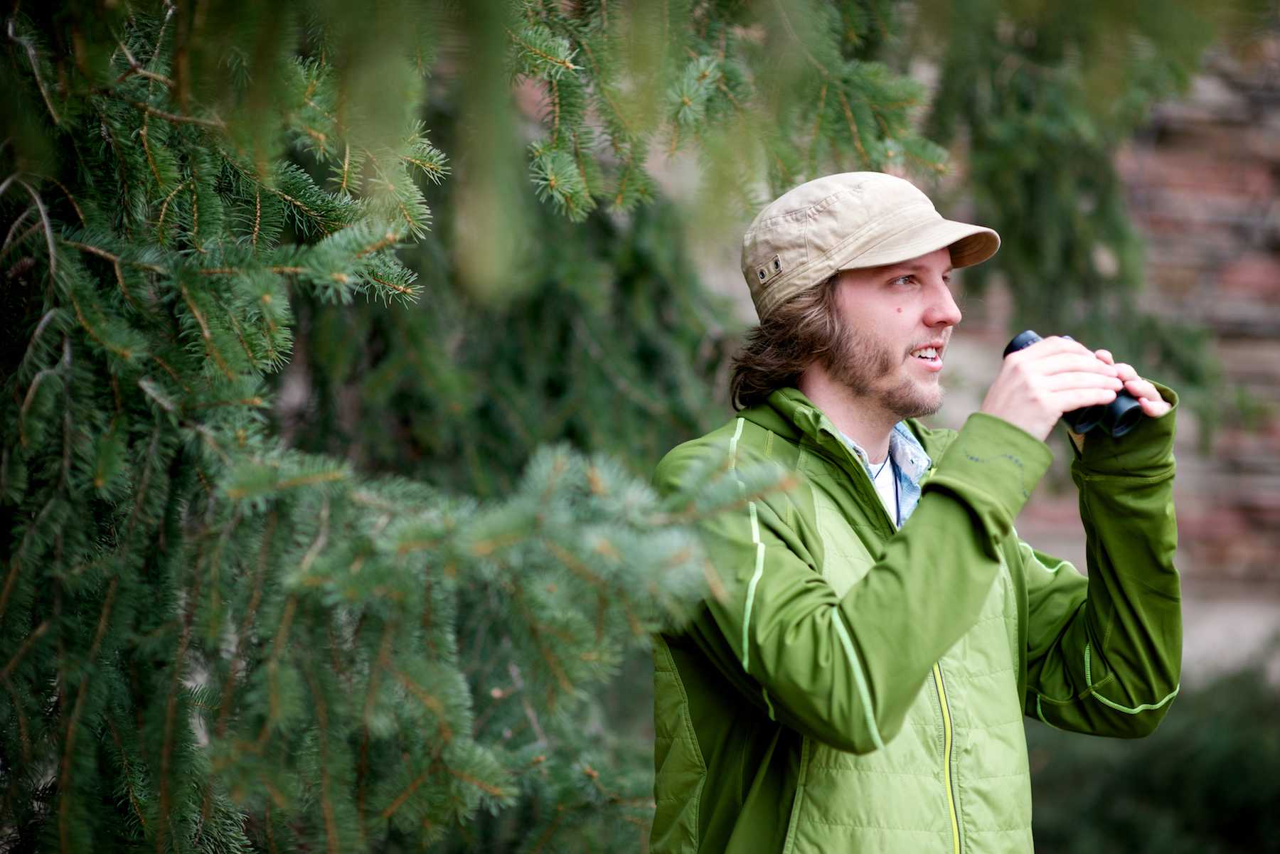 Adam miller, a senior wildlife biology major, uses binoculars to identify birds from their site and call in the Monfort Quadrangle. Miller has been involved in undergraduate research since freshman year and is currently studying how housing development affects bird nesting patterns.