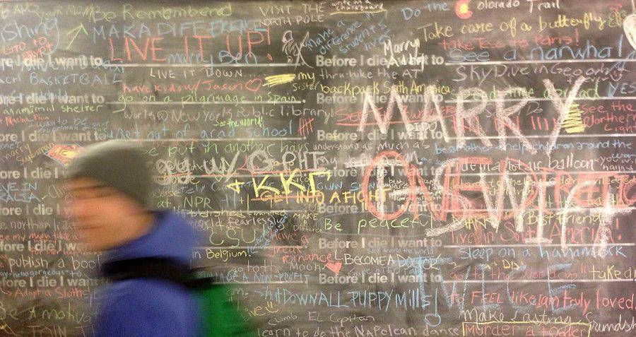 Freshman Business Administration major Cooper Denny walks past the filled Before I Die walls in the Lory Student Center Tuesday. Anyone can walk up and finish the phrase Before I die I want to... in chalk on the board. There are over 100 similar walls around the world, but only two are located in Colorado.