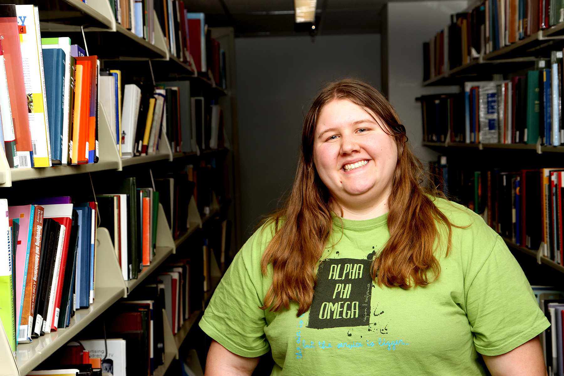 Junior Honors student, Adara Schweikart, stands by the very books that aided her with her pages and pages of work for her Honors thesis. Schweikart, along with many other Honors students, recently presented her thesis.