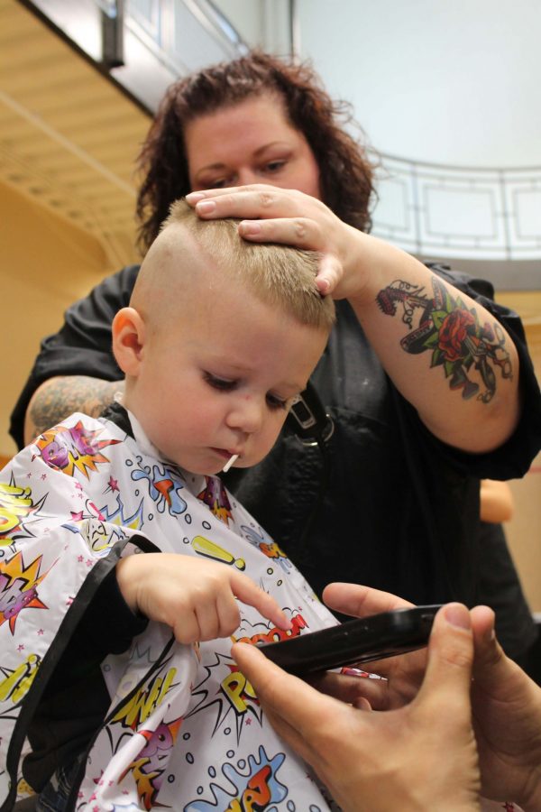 Three year old Fort Collins resident, Gage, plays on his dad's phone while getting a hair cut at the Aztlan Community Center. Project Homeless Connect was a one day volunteering event that provided families in need with a variety of resources to help them get back on their feet.