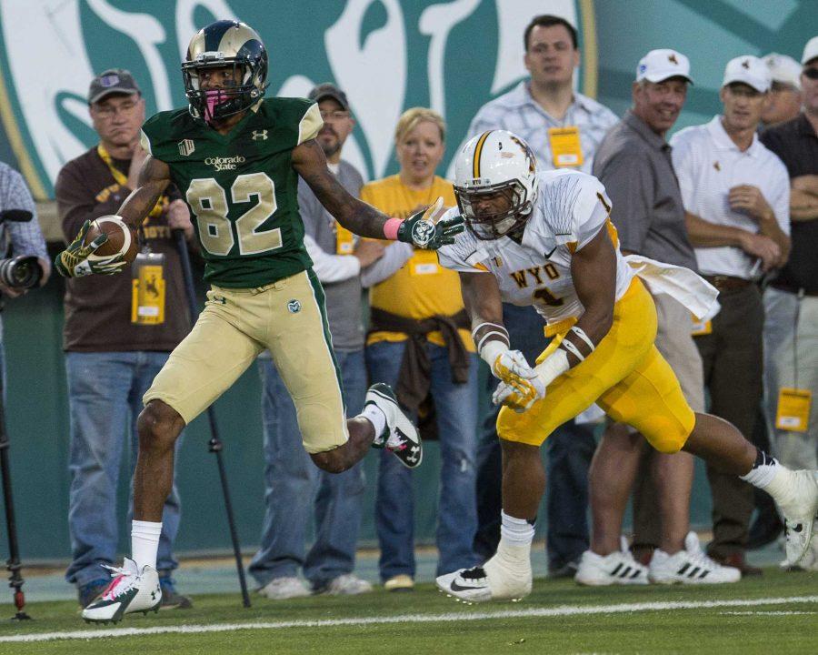 One football player runs with the ball in his hand while a player from the other team runs behind him, barely missing catching him.