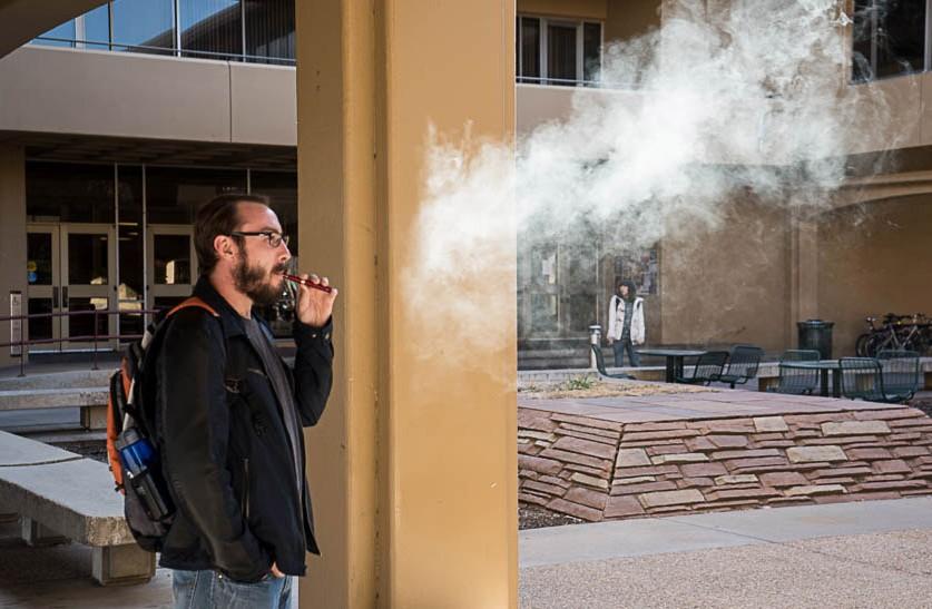 Senior psychology major, Jeff Cox takes a puff on his e-cigarette between classes under the Clark Building at Colorado State University. (Photo credit: Zane Watson)