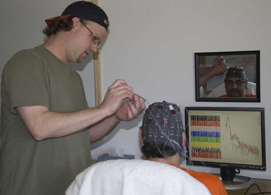 (From left) Elliott Forney, a graduate computer science student, meticulously applies gel to Fereydoon Vafaei, computer science doctoral candidate, to ensure a solid connection to collect electroencephalograms, or, EEG for short. Both are part of a study where the long-term goal of the research is a new mode of communication for victims of diseases and injuries that will lead to a stable and healthy control of muscle movement. (Photo credit: Kevin Olson)