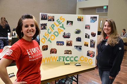 Lexy Bushue a Freshman chemical engineering major, left, and animal/equine science major Katrina Mulroy stand to promote Disciples Today at the faith fair on Monday.