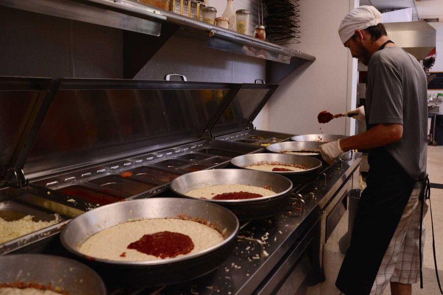 Krazy Karl's employee James Gilbert spreads sauce over several pizza crusts. Gilbet said he likes the work environment in the pizza shop because the people are fun to work with and the work environment is laid back but he has enough work to keep him busy. (Photo Credit: Megan Fischer)