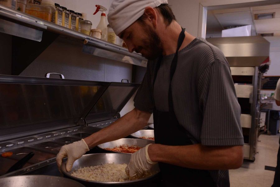 James Gilbert spreads cheese over several pizza crusts at Krazy Karl's pizza on West Elizabeth Street. According to Gilbert, he likes the work environment in the pizza shop, saying the people are fun to work with and the work environment is laid back but he has enough work to keep him busy. (Photo Credit: Megan Fischer)