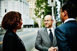 Three colleagues in discussion on sidewalk of city street