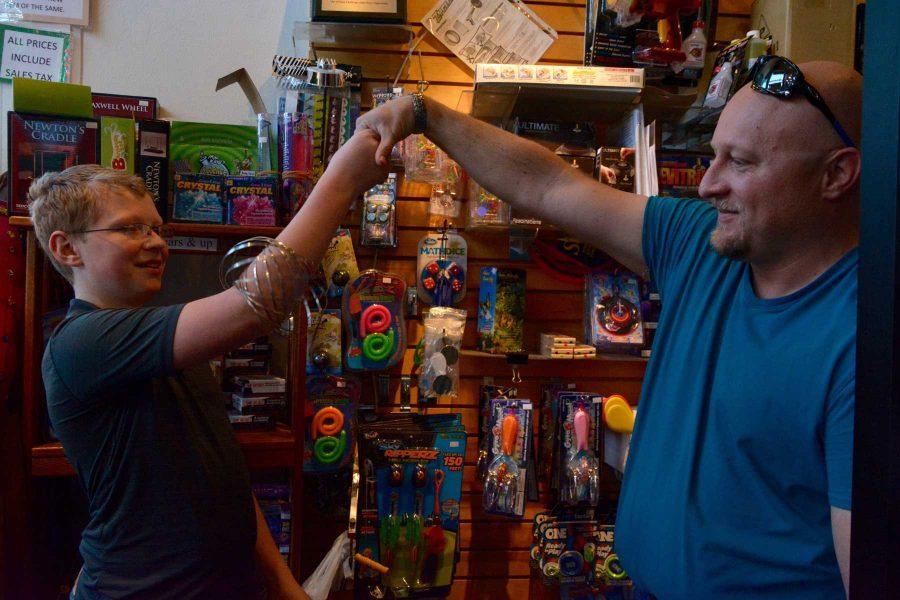 Jeremy Sundberg (right) and son, Hunter, 13 shake hands to transfer one of the science toys in Science Toy Magic, located in Old Town Square, Fort Collins. (Photo Credit: Megan Fischer)