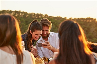 Smiling couple watching photographs on smart phone at dinner party
