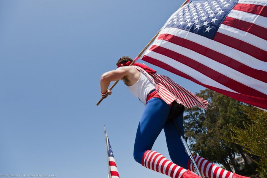 Young man on unicycle with American flag. People at Morro Bay, C