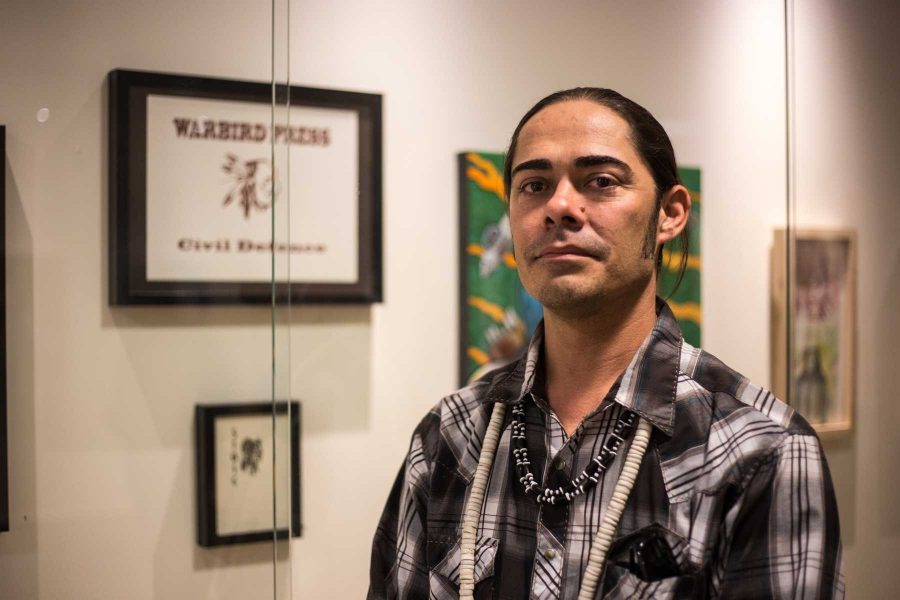 Native American artist Jacob Meders stands in front of his art on display durring the #HandsOffMyHeritage event in the LSC Thursday Nov.10. Photo credit: Ryan Arb