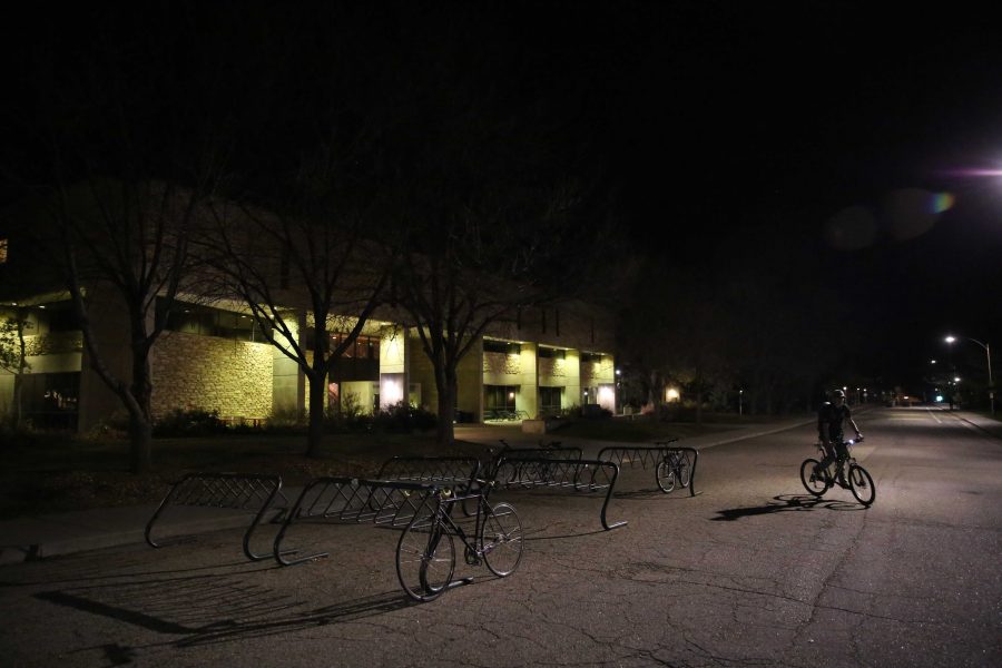 A Colorado State University student rides his bike past the nearly empty bike racks in front of the Warner College of Natural Resources at night earlier this week. (Forrest Czarnecki | Collegian)