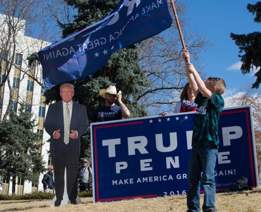Brycen Thomas waves a Trump flag while his parents, Ryan and Chelsea Thomas, hold a large sign at the March 4 Trump rally in Denver on Saturday. Photo by Kaitlyn Ancell | Collegian