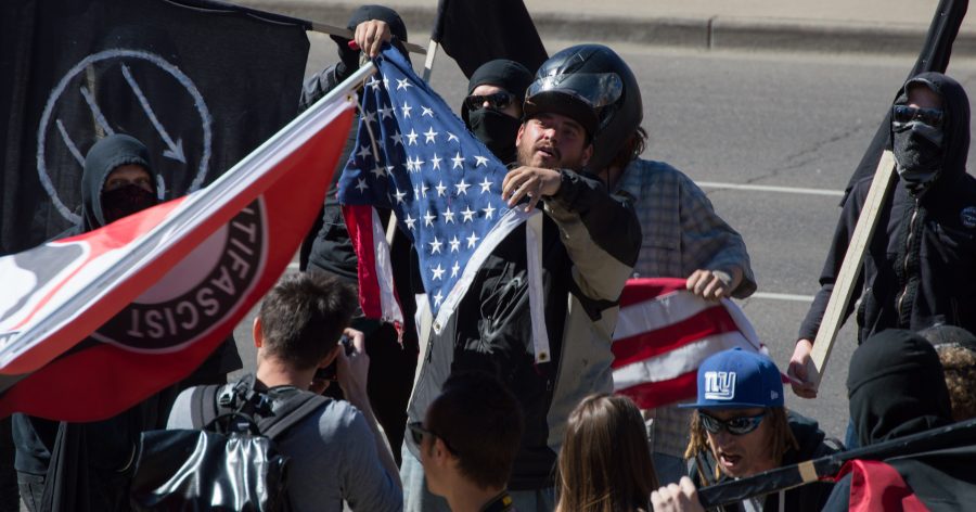 The ANTIFA protestors rip a flag in a demonstration against Trump at the March 4 Trump rally in Denver on Saturday. Photo by Kaitlyn Ancell | Collegian