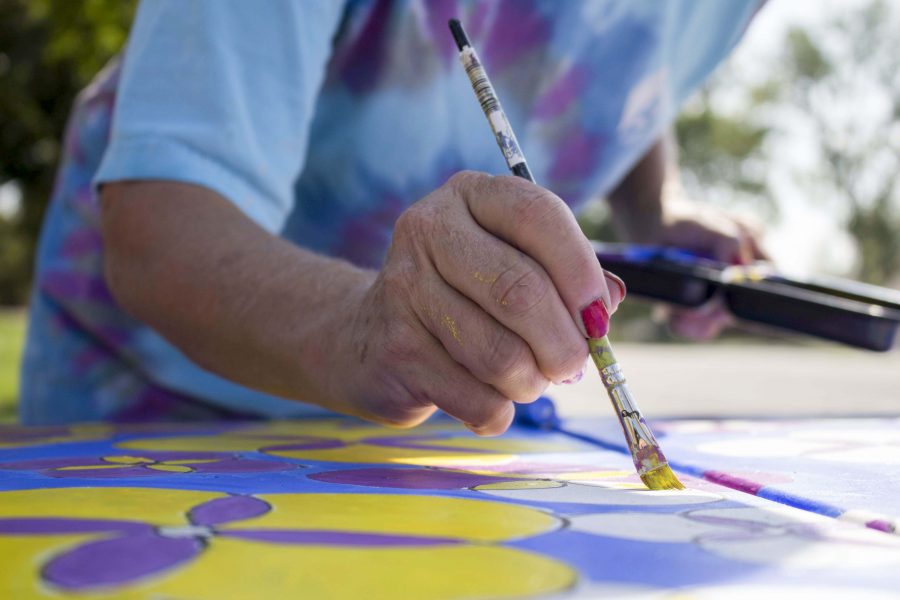 Sharon Smith paints an electrical box with yellow and purple flowers for the Transformer Cabinet Mural Project last Sunday. The project seeks local artists to paint over graffitied objects around Fort Collins. (Broke Buchan | Collegian)
