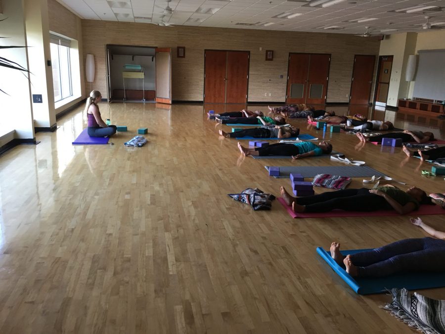 Students complete Yoga class with relaxing pose reclined on mats while instructor, Carly McGowan sits in front of the class directing movement. Photo credit: Emma Turner