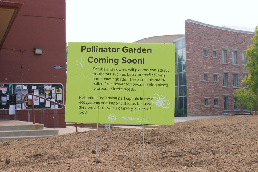 A pollinator garden sign stands in a pile of dirt near The clark Building. 