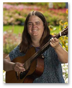 Ellen Audley playing guitar outside surrounded by flowers