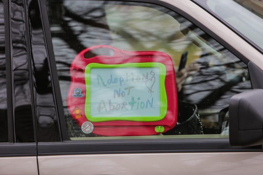 A hand-drawn sign reading Adoption Not Abortion is held up to a car window on its way into the Republican Party fundraiser where U.S. Vice President Mike Pence would be speaking. (Davis Bonner | Collegian)
