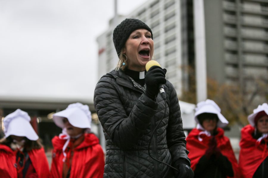 Rev. Amanda Henderson speaks to the crowd of protestors dressed as handmaids gathered outside the Denver Marriott Tech Center where Vice President Mike Pence is to give a speech at a Republican Party fundraiser. The costumes are in reference to the popular television show Handmaids Tale that describes a world in which women are considered property. (Davis Bonner | Collegian)