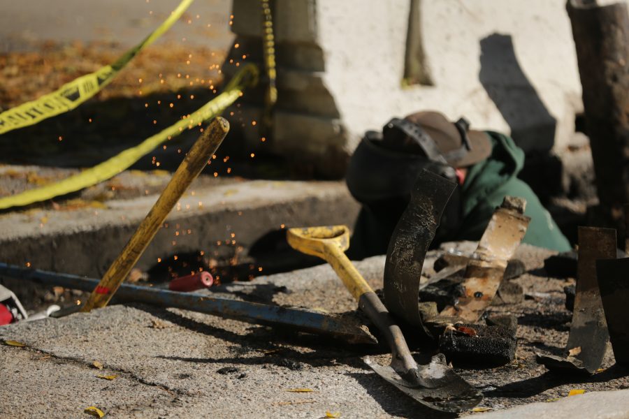 Metal strips and construction equipment are strewn around a construction zone while a construction worker welds a pipe along West Plum Street near the Colorado State University Transit Center on Tuesday morning. Workers were replacing and rerouting a condensation line underneath the roadway. (Forrest Czarnecki | The Collegian)