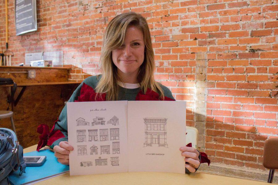 Emma St. Aubin holds up two of her drawings. She sells her pieces on her Etsy shop, Saint Aubin Ink. Many of her pieces feature buildings from Fort Collins. (Ashley Potts | Collegian)