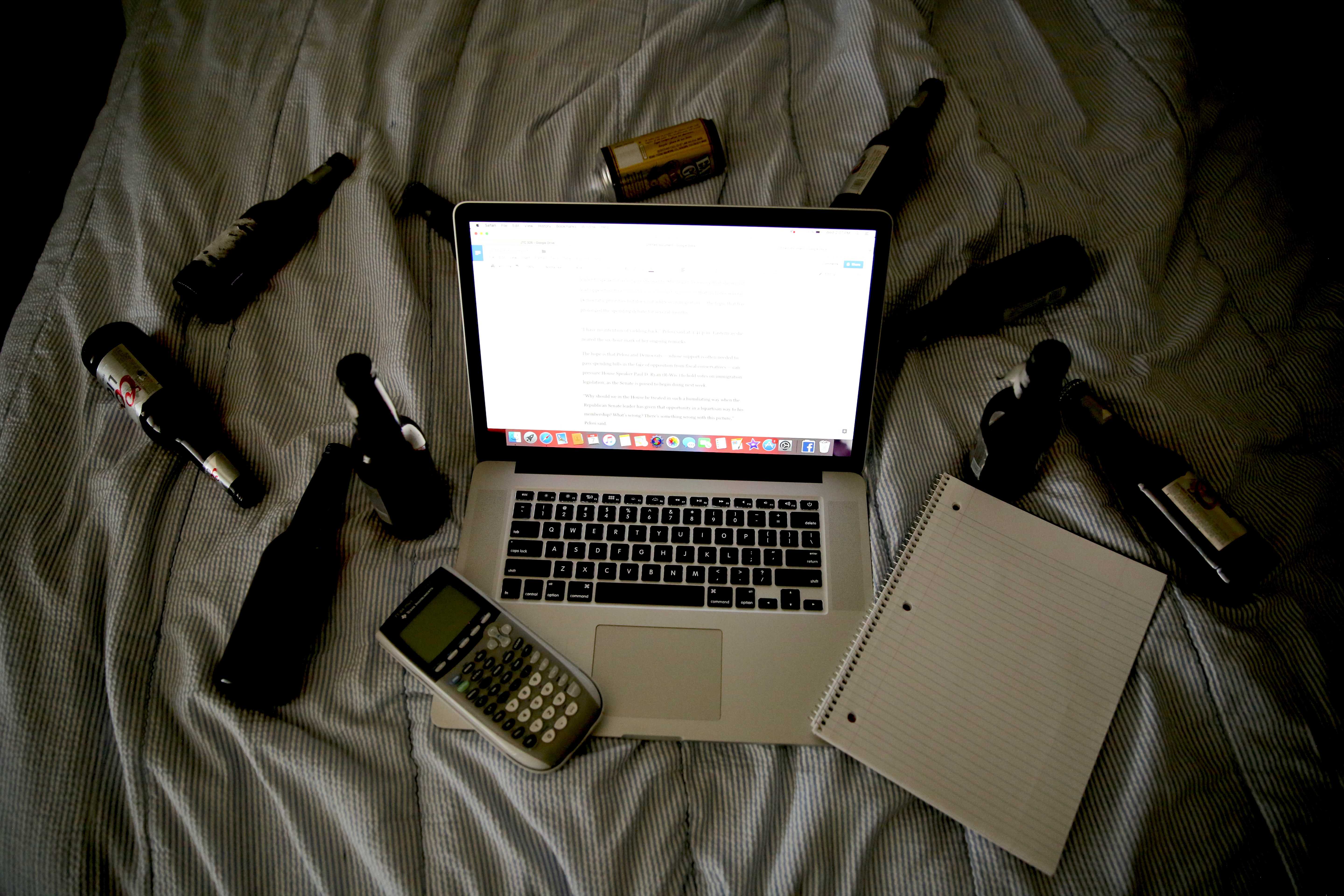 Beer bottles and cans sit next to a computer and notebook on a bed.