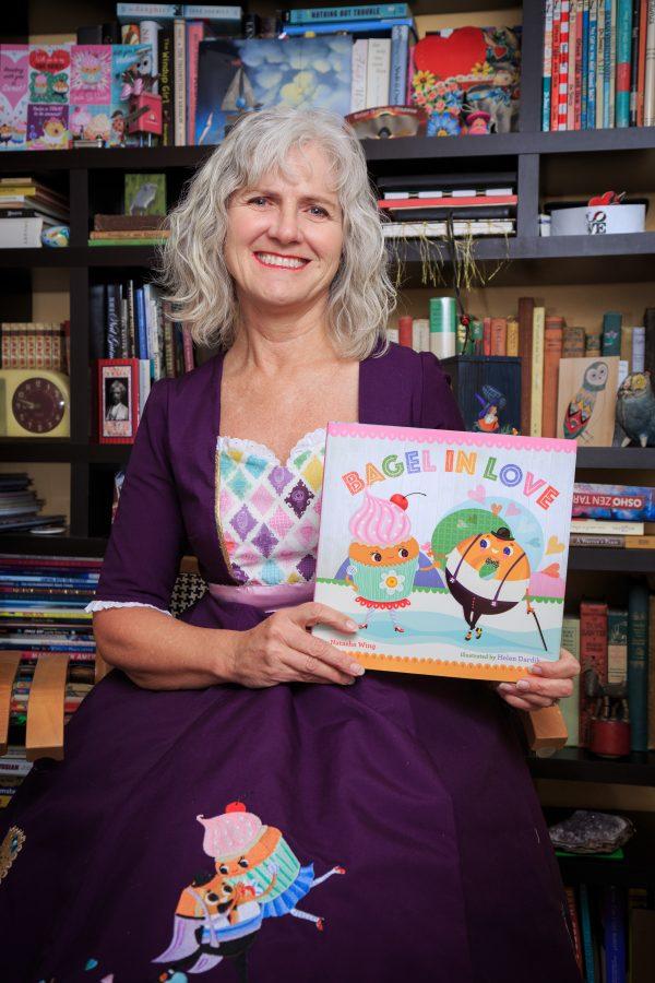Natasha Wing, a Fort Collins based childrens book author, holds her recent book Bagel in Love that served as the primary inspriation behind her custom dress made by CSU student Cameron Utter. (Davis Bonner | Collegian)
