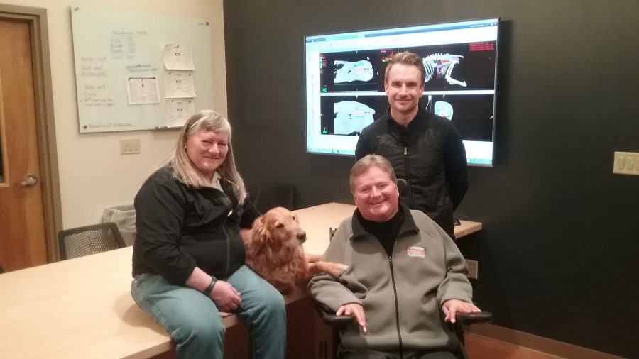 Nan Stuart (left), Kelsey (dog), Sam Schmidt (middle) and Jay Howard (right) pose for a photo in the Flint Animal Cancer Center. (Mack Beaulieu | Collegian)