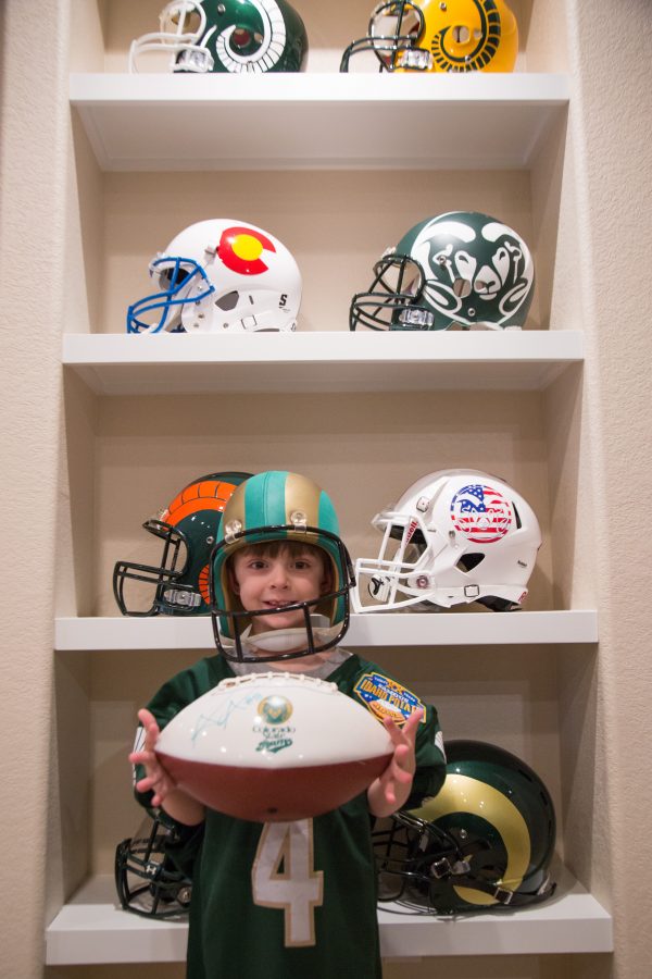 Bryce Krisl stands in front of his fathers custom helmets wearing the signed jersey given to by Colorado State wide receiver Michael Gallup. Krisl has been attending CSU home games since he was two months old. (Davis Bonner | Collegian)