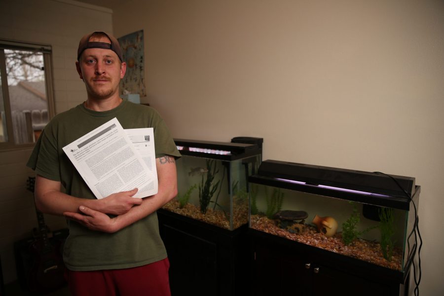 Chris Kopack holds research papers of his and poses for a portrait inside his home office in Fort Collins, where he keeps two large aquariums with freshwater fish species from his graduate work. The fish Kopack has at his home are muskelunge, which are large predatory fish, and Arkansas Darters, a smaller fish thats native to Colorado. Kopack was recently awarded a fellowship from the National Science Foundations Graduate Research Fellowship Program that will help him continue his graduate research. Kopack is doing his graduate work on native fish species in Colorado.  (Forrest Czarnecki | The Collegian)
