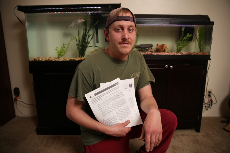 Chris Kopack holds research papers of his and poses for a portrait inside his home office in Fort Collins, where he keeps two large aquariums with freshwater fish species from his graduate work. The fish Kopack has at his home are muskelunge, which are large predatory fish, and Arkansas Darters, a smaller fish that's native to Colorado. Kopack was recently awarded a fellowship from the National Science Foundation's Graduate Research Fellowship Program that will help him continue his graduate research. Kopack is doing his graduate work on native fish species in Colorado.  (Forrest Czarnecki | The Collegian)