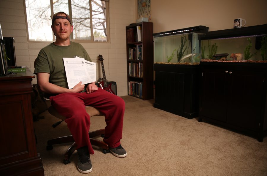 Chris Kopack holds research papers of his and poses for a portrait inside his home office in Fort Collins, where he keeps two large aquariums with freshwater fish species from his graduate work. The fish Kopack has at his home are muskelunge, which are large predatory fish, and Arkansas Darters, a smaller fish that's native to Colorado. Kopack was recently awarded a fellowship from the National Science Foundation's Graduate Research Fellowship Program that will help him continue his graduate research. Kopack is doing his graduate work on native fish species in Colorado.  (Forrest Czarnecki | The Collegian)