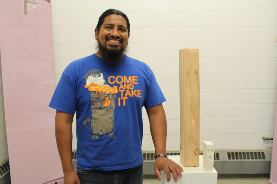 Construction materials are not just made for labor, Saxon Martinez emphasizes. For his current assignment, he is using materials such as concrete, wood, and foam installation boards. These materials can be made into art, and Martinez plans to use them as such, depicting his Latino heritage and the stereotypes that come with it. Here, Martinez poses with the beginning stages of his installation set up. (Sarah Ehrlich | Collegian)