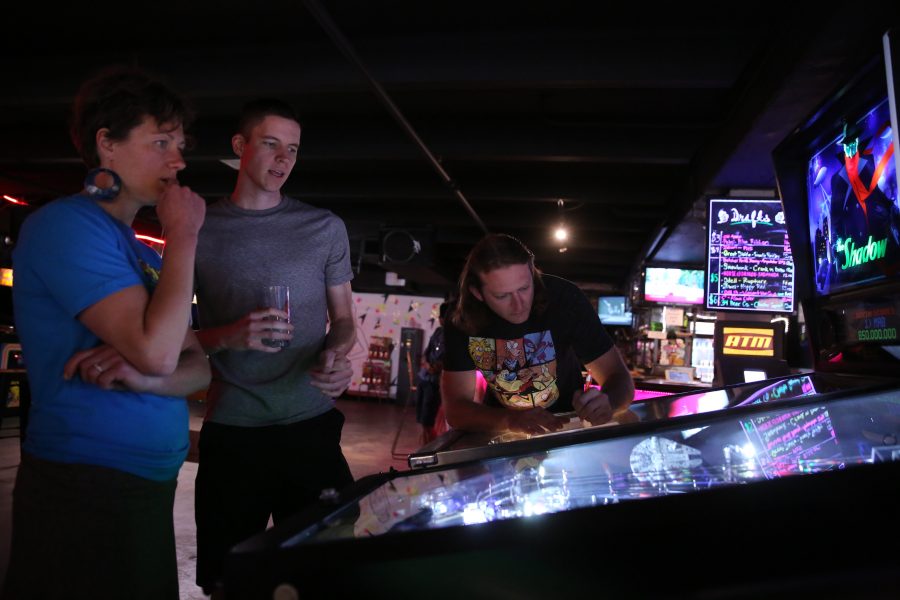 Natasha Kalda, left, and Elliott Layne discuss pinball tactics and the intricacies of pinball machines while Jcob Kalda, right, writes down his score following a game of pinball at the Pinball Jones Campus West location.  (Forrest Czarnecki | The Collegian)