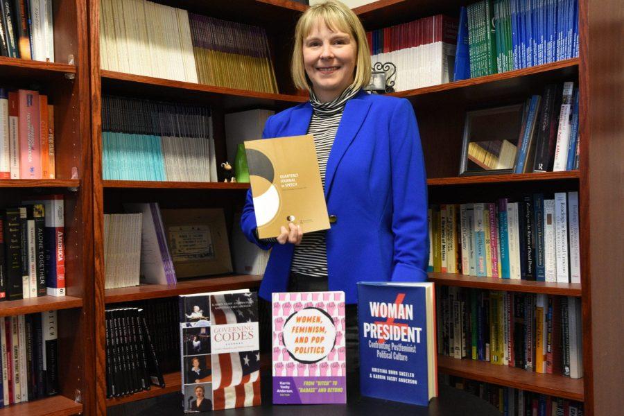 Communication Studies Professor Karrin Anderson, poses for a photo with the three books she has written while holding the scholarly journal she is reviewing. Anderson primarily writes about 
