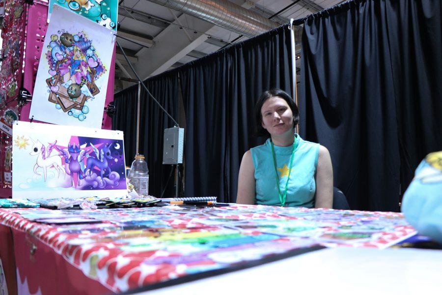 Kayla Wilson smiles while sitting infront of her booth surrounded by her artwork that's for sale. (Devin Cornelius | Collegian)