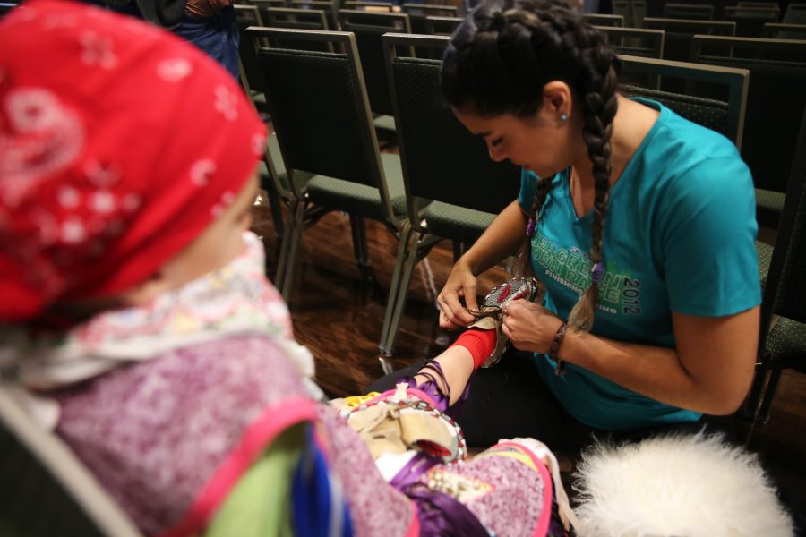 Cetan Christensen, right, helps put a moccasin on Tate Christensen's foot before the start of the 36th annual AISES Pow Wow at the LSC on Nov. 3, 2018. The moccasin was made by Cetan's mother, and has been passed down to Tate. (Forrest Czarnecki | Collegian)