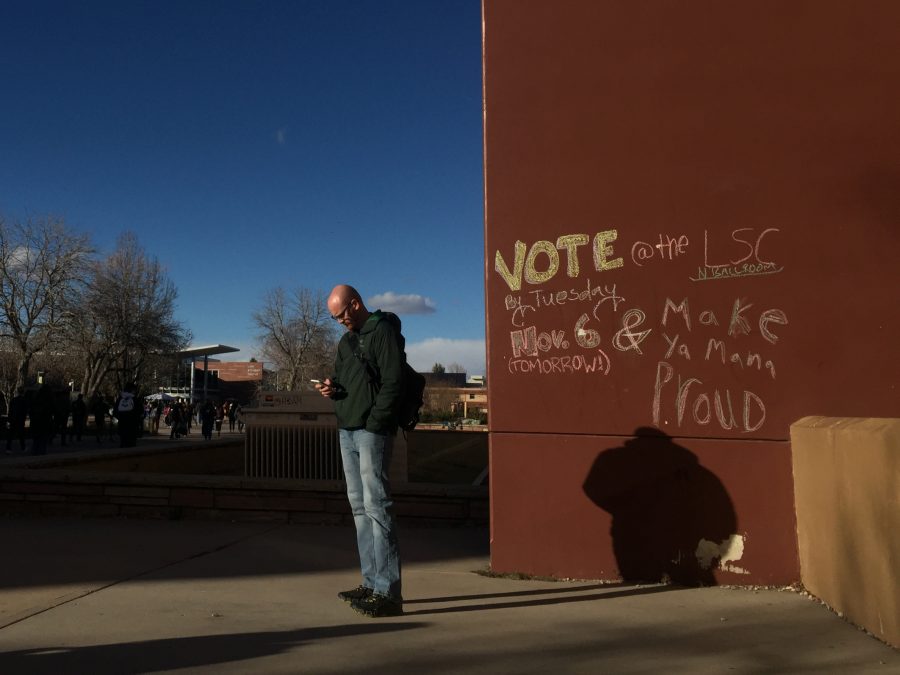 A chalk-drawn message encouraging students to submit their ballots is pictured on the side of the Clark A building while a Colorado State University student checks his phone on Nov. 5, 2018. Tuesday, Nov. 6 is the last day to submit voting ballots across the state. (Forrest Czarnecki | Collegian)