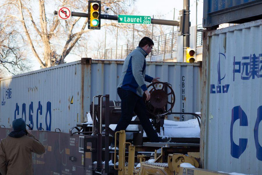 A pedestrian crosses the cars of a stopped freight train near the intersection of Mason and Laurel streets following a train and pedestrian collision at 2:57 p.m. Feb. 7. One fatality was confirmed by Fort Collins Police Services. (Austin Fleskes | Collegian)