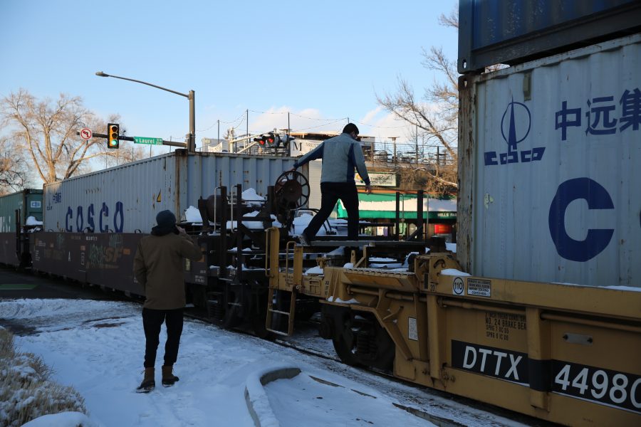 Pedestrians cross in between the cars of a freight train that is stopped near the intersection of Mason and Laurel streets following a collision with a pedestrian at approximately 2:57 p.m. Feb. 7. One fatality was confirmed by Fort Collins Police Services. (Forrest Czarnecki | Collegian)