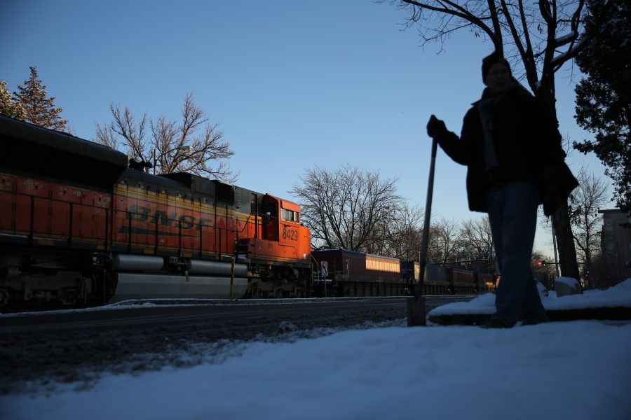 Greg Taylor clears snow from the sidewalk in front of his store while a stopped freight train sits near the intersection of Mason and Mulberry streets following a train and pedestrian collision at approximately 2:57 p.m. Feb. 7. One fatality was confirmed by Fort Collins Police Services. (Forrest Czarnecki | Collegian)