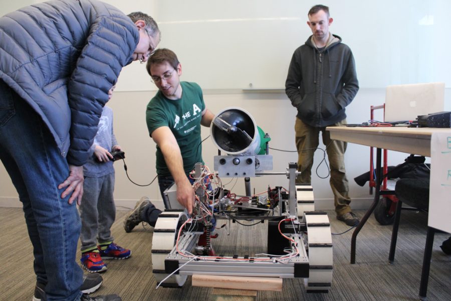 Jeff Larchar, a Senior Mechanical Engineer major here at Colorado State, lets a father and a son handle an experimental rover during the Little Shop of Physics Open House. (Joshua Contreras | Collegian).